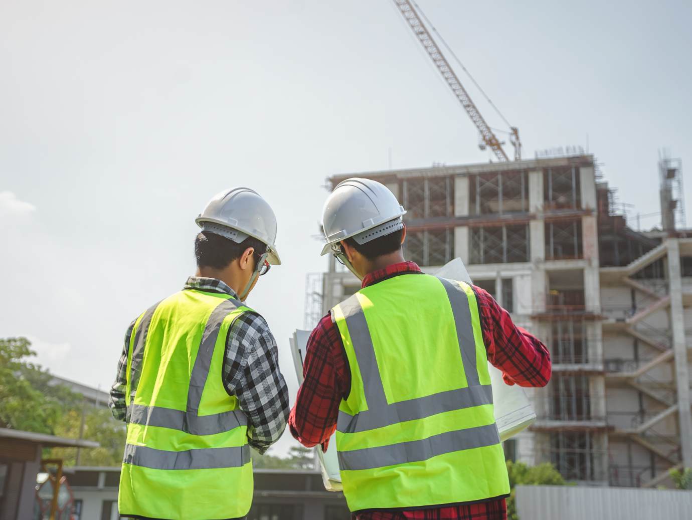 Two engineers in vests discuss technical consultancy plans for an industrial facility at a construction site